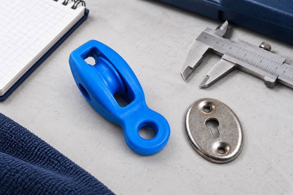 Nylon pool pulley and oval keyhole plate beside a vernier caliper for replacement identification